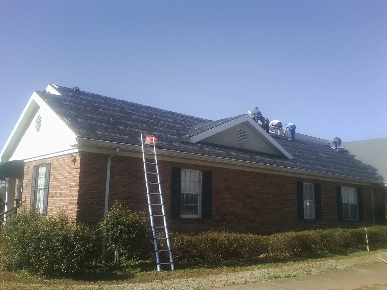 Crew tearing shingles off a brick ranch roof with a ladder set — Emergency Roof Repair work by our crew in Lancaster