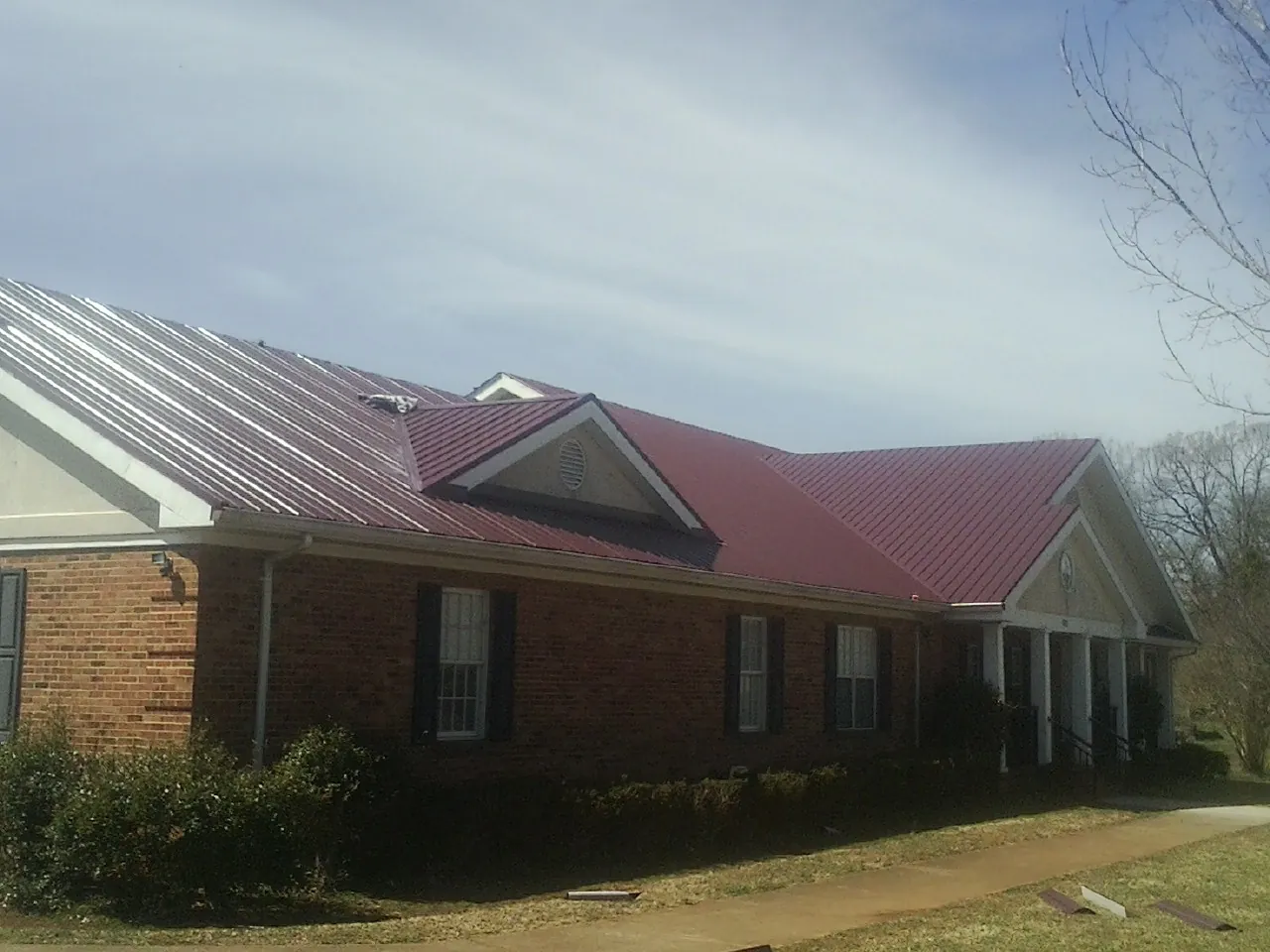 Red metal roof with gabled entries on a long brick building, from a Hail Damage Roof Repair job in Lancaster