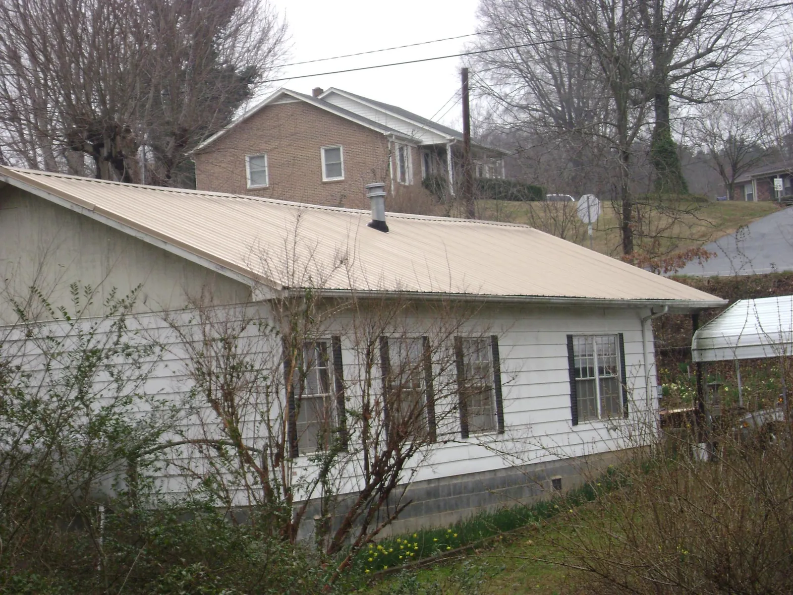 Tan metal roof on a white sided house set into a hillside — Commercial Roofing by Roofing Brothers in Lancaster